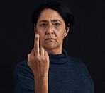 Portrait, anger and senior woman with middle finger, opinion and expression on a black studio background. Face, female person and old model with gesture, rude and frustrated with problem and conflict