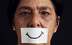 Portrait, smile or anxiety and a mature woman in studio on a dark background with a fake expression. Depression, abuse and mental health with a female person looking brave to hide her emotions