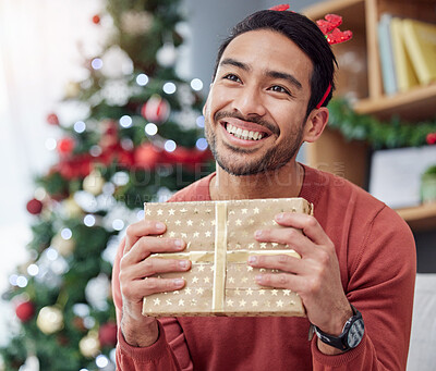 Buy stock photo Christmas, smile and asian man with gift in his home happy, excited and having fun holiday celebration. Hand holding, box and Japanese male with present in a living room at December party or event