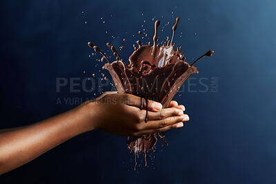 Chocolate, splash and candy with hand of person in studio for cocoa, dessert and sugar. Confectionary, sweets and treat with closeup of model and on blue background for movement, ingredients and drop