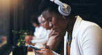Headphones, phone and woman at cafe listening to music, remote work and networking on social media. African person in workspace, restaurant or coffee shop with mobile chat and audio streaming service