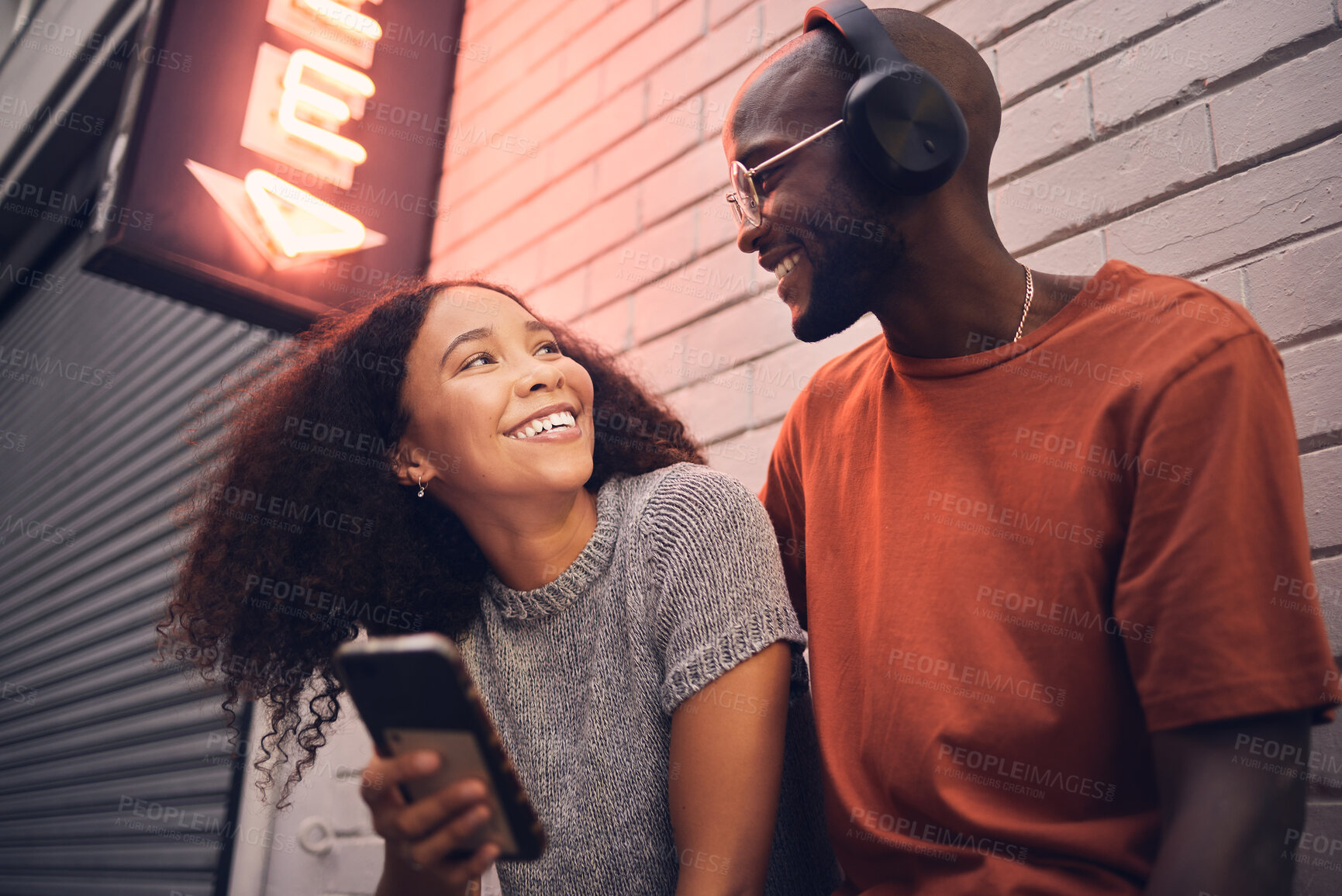 Buy stock photo Phone, music and headphones with an interracial couple outdoor in a city together for dating. Love, mobile app or streaming with a man and woman bonding in an urban town while listening to the radio