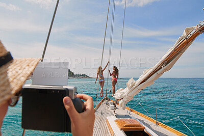 Buy stock photo Two happy friends in bikinis on holiday cruise together having their photo taken. Woman taking photos of two young women on holiday on boat cruise together with vintage photography camera