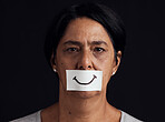 Portrait, smile or abuse and a mature woman in studio on a dark background with a fake expression. Depression, anxiety and mental health with a female person looking brave to hide her emotions