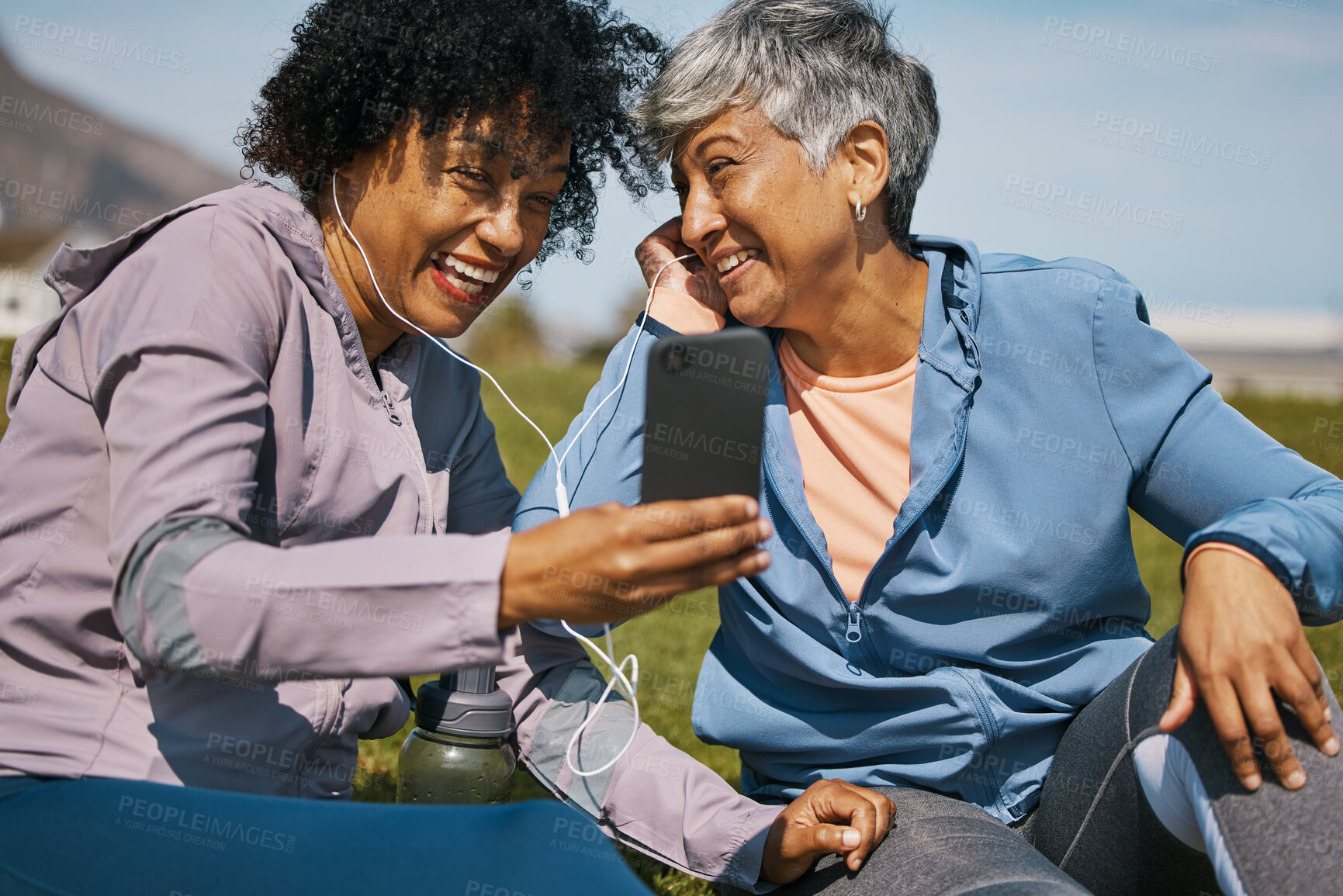 Buy stock photo Phone, fitness and music with senior friends on the grass outdoor taking a break from their workout routine. Exercise, smile and elderly people streaming audio while laughing on a field for wellness