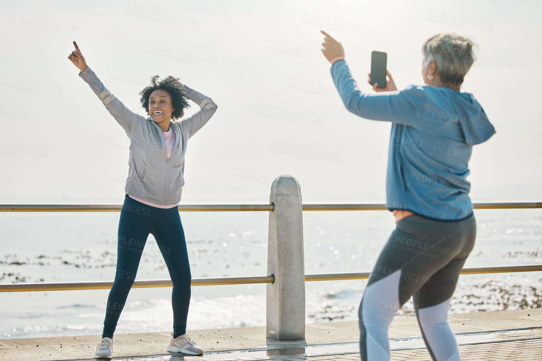 Buy stock photo Photograph, senior woman and friends fitness with social media post feeling silly by the sea. Training, exercise and workout with mature people and photo for profile picture with pointing by ocean