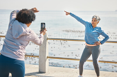 Buy stock photo Phone, friends and photo of senior woman pointing at beach with silly pose at sea for fitness. Exercise, mobile and picture for social media post on a ocean promenade walk for workout and friendship