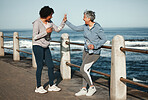 Fitness, high five and senior women by ocean for healthy lifestyle, wellness and cardio on promenade. Sports, friends and female people celebrate on boardwalk for exercise, training and workout goals