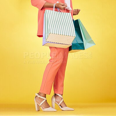 Buy stock photo Legs, woman and shopping bag in studio for fashion, retail deal and financial freedom on yellow background. Closeup of customer, gift bags and discount from clothes store, shoes sales and promotion