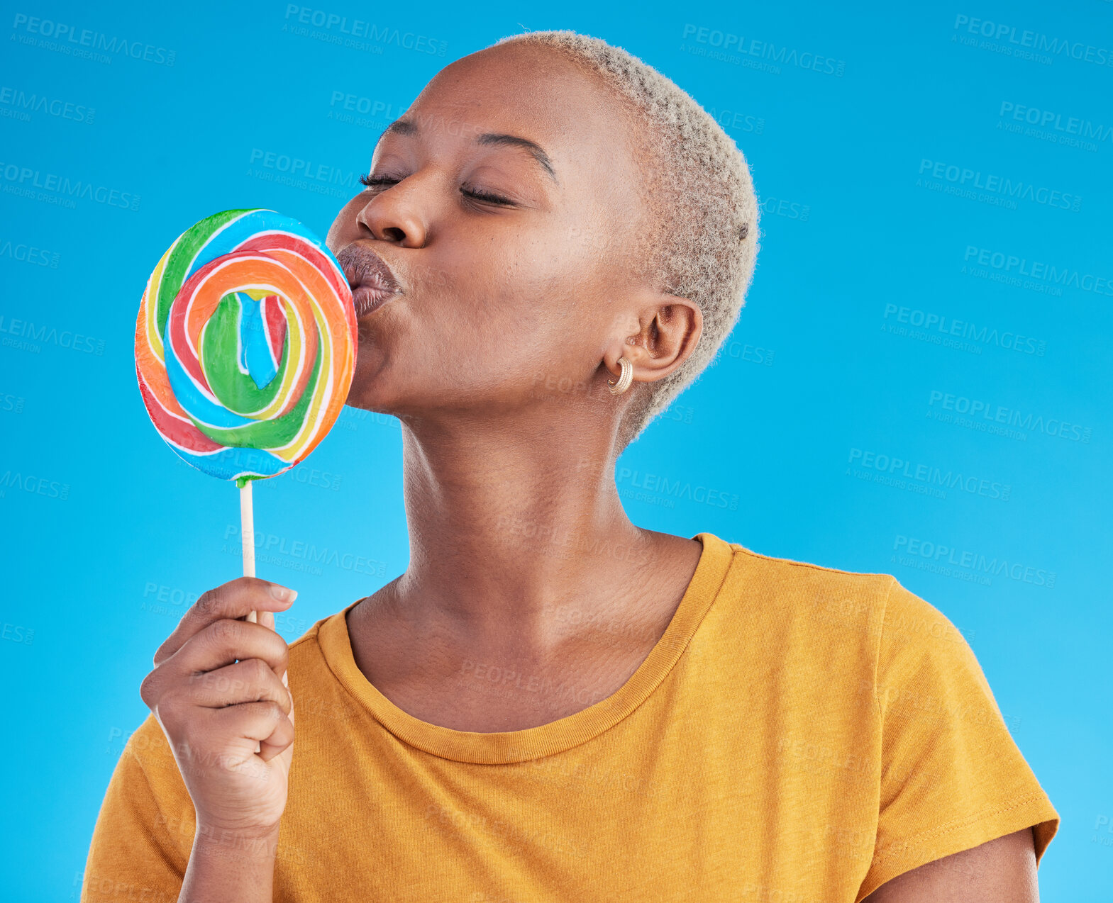 Buy stock photo Lollipop, kiss and a woman with candy in studio for sweets, rainbow and creative advertising. Happy and funny black female person isolated on a blue background with love of sugar, freedom and color