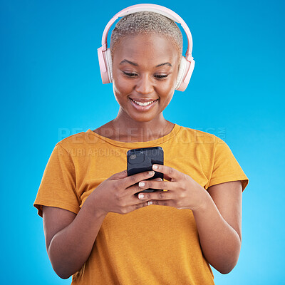 Buy stock photo Woman, smartphone and headphones listening to music, audio streaming service or social media on blue background. Young african person or influencer chat on mobile for podcast subscription in studio