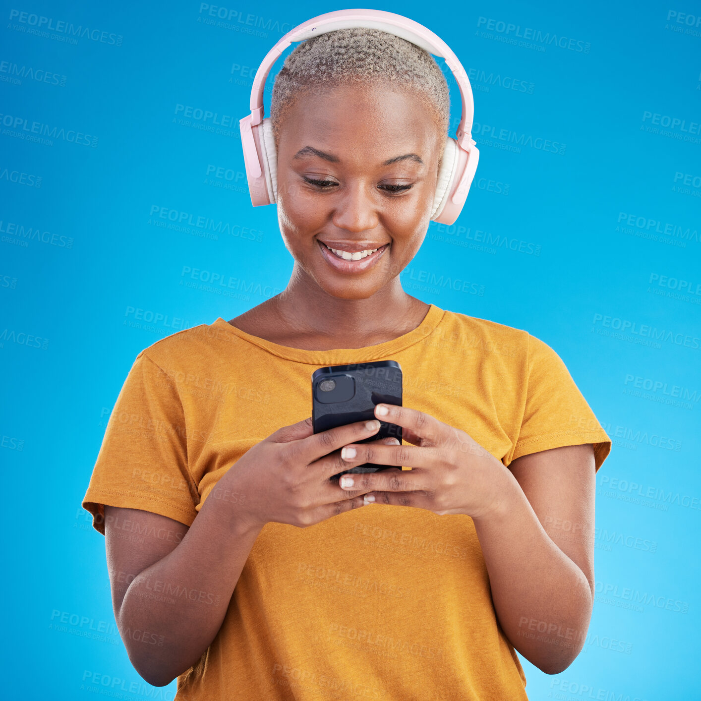 Buy stock photo Woman, smartphone and headphones listening to music, audio streaming service or social media on blue background. Young african person or influencer chat on mobile for podcast subscription in studio