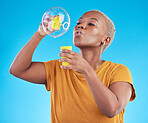 African, woman and blowing bubbles in studio, blue background or party celebration with fun, liquid soap or toy. African girl, person and relax with happy, joyful or creative bubble for calm break