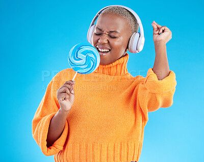 Buy stock photo Music headphones, lollipop or black woman listening to radio playlist to relax on blue background in studio. Sweets, candy or girl singer dancing, singing or streaming a song audio or sound track 