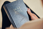 Bible, hands and person in prayer, religion and peace in a lounge, praise and holy worship for guidance. Closeup, believer or faith with meditation, reading book or mindfulness with spiritual or calm