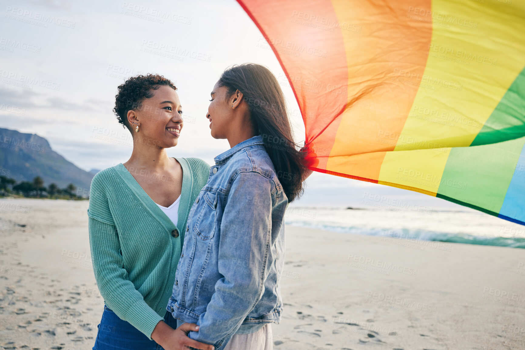 Buy stock photo Gay, flag and lesbian couple at the beach for travel, freedom and bond, care and happy in nature together. Rainbow, love and women on ocean vacation embrace lgbt, partner or pride, date or acceptance