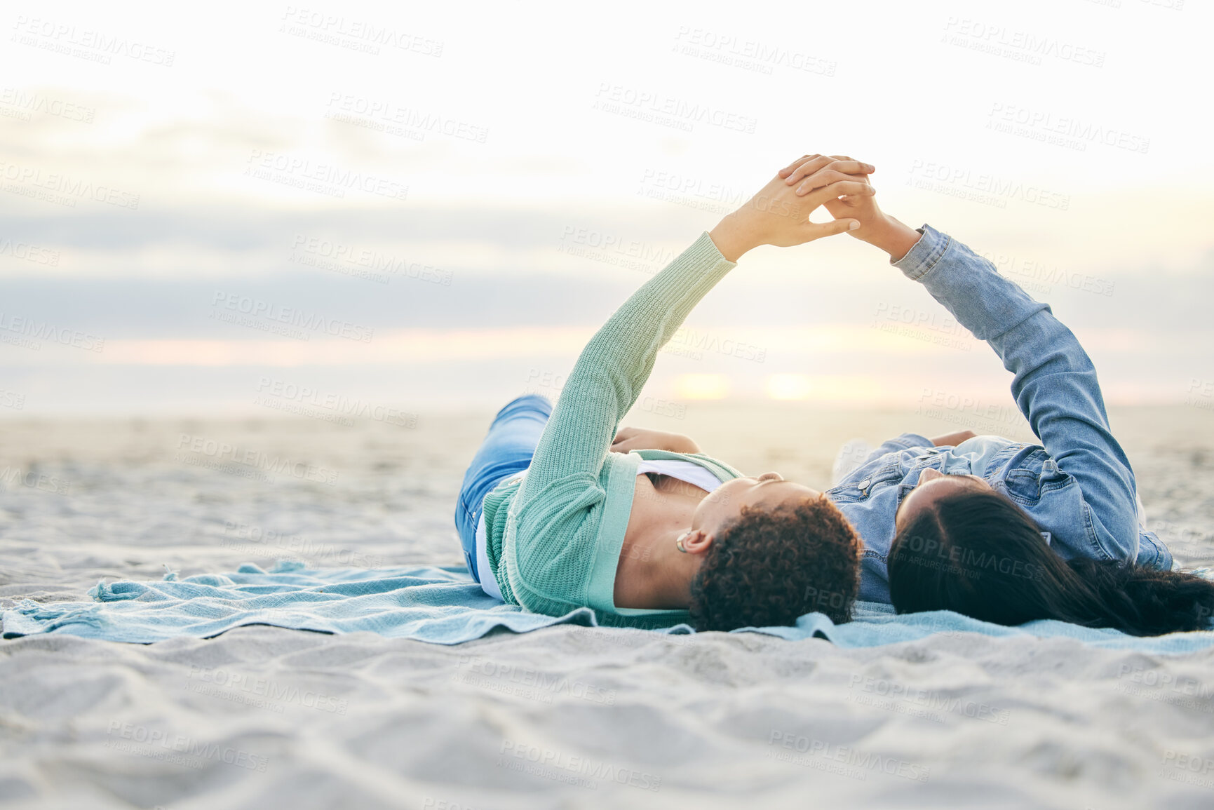 Buy stock photo Love, beach and lesbian couple on blanket together, holding hands on sand and sunset holiday adventure. Lgbt women, bonding and relax on ocean vacation with romance, pride and happy lying in nature.