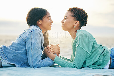 Buy stock photo Love, ocean and sunset, lesbian couple on blanket together, holding hands on sand and holiday adventure. Lgbt women, bonding and relax on beach vacation with romance, pride and happy lying in nature.