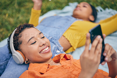 Buy stock photo Music, phone and lesbian couple relax at picnic on grass, technology and streaming service app in nature. Cellphone, listening to headphones and happy lgbt women on blanket in garden together in park