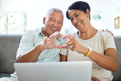 Buy stock photo Mature couple, heart hands and laptop on home sofa for video call, streaming and internet. A happy man and woman together on a couch with technology for communication, social media emoji or love