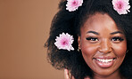 Flowers, face and black woman in afro hair care, smile and beauty in studio isolated on a brown background mockup space. Portrait, floral hairstyle cosmetic and natural African model in organic salon