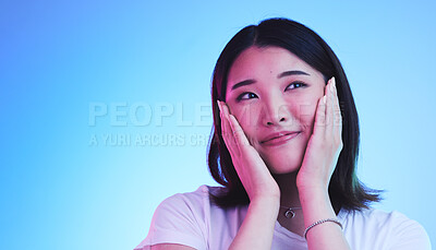 Buy stock photo Face, thinking and Asian woman with beauty or dream with hope or smile isolated in a studio blue background. Cute, shy and happy young female person with skincare or soft skin and with a memory