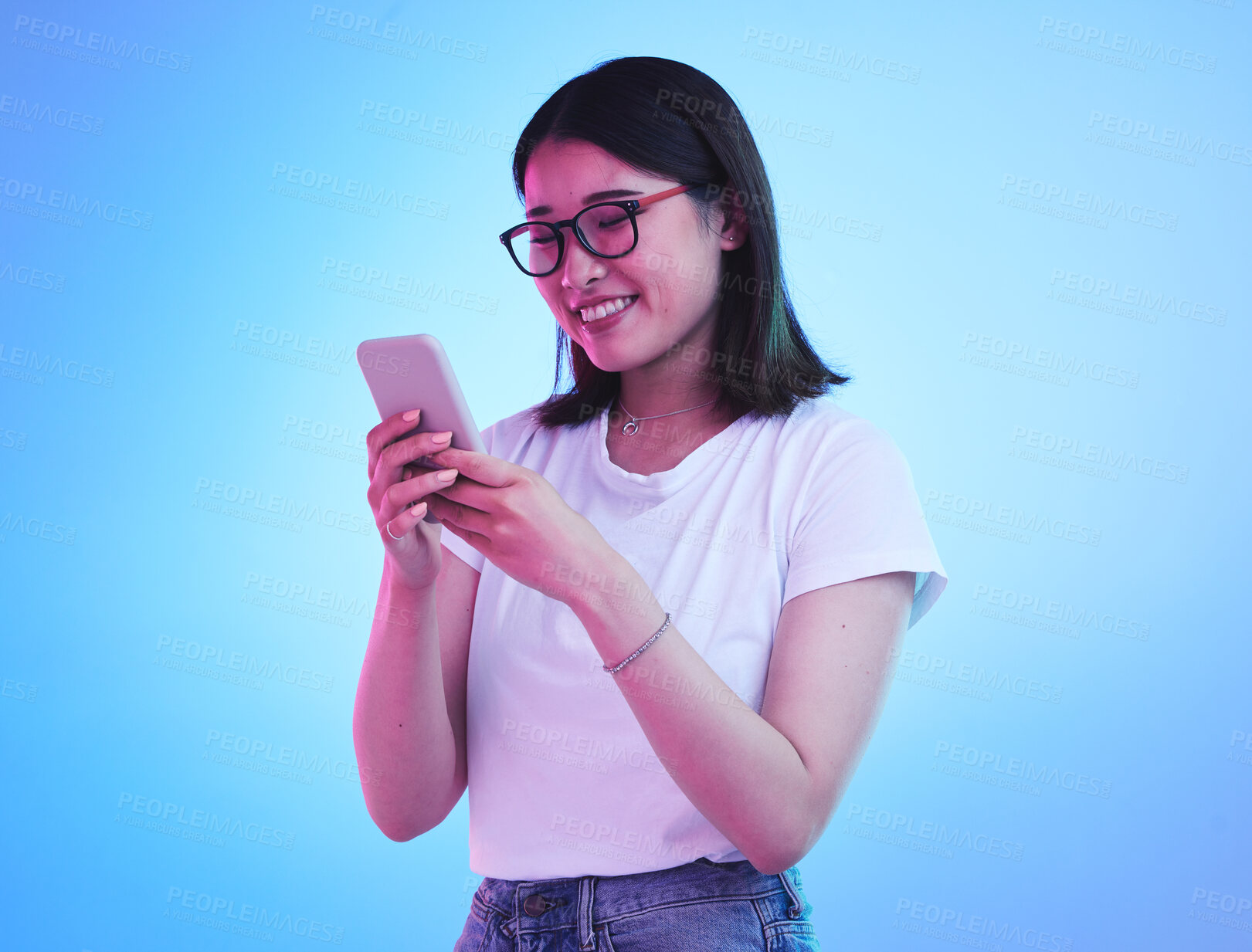 Buy stock photo Phone, typing an Asian woman on social media with mobile app, internet or web isolated in a studio blue background. Connection, cellphone and young female chatting with smile for communication