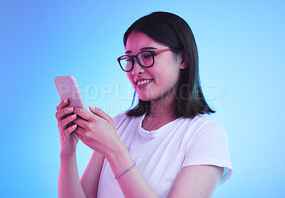 Buy stock photo Phone call, reading an Asian woman in conversation on mobile app to contact person online in studio blue background. Connection, cellphone and young female chatting with smile for communication