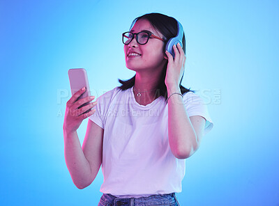 Buy stock photo Woman, student and phone with headphones listening to music, techno streaming and radio on blue background. Person, gen z or youth audio, electronics and mobile subscription in neon light and studio