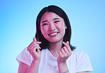 Love, hands and portrait of Asian woman in studio with smile for romance, valentines day and happy. Emoji, neon lighting and face of person with hand gesture, finger sign and smile on blue background