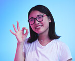 Woman, okay hands or sign for learning success, certified and excellence in tshirt and a blue, studio background. Happy young, asian person in glasses, portrait and yes or support emoji for education