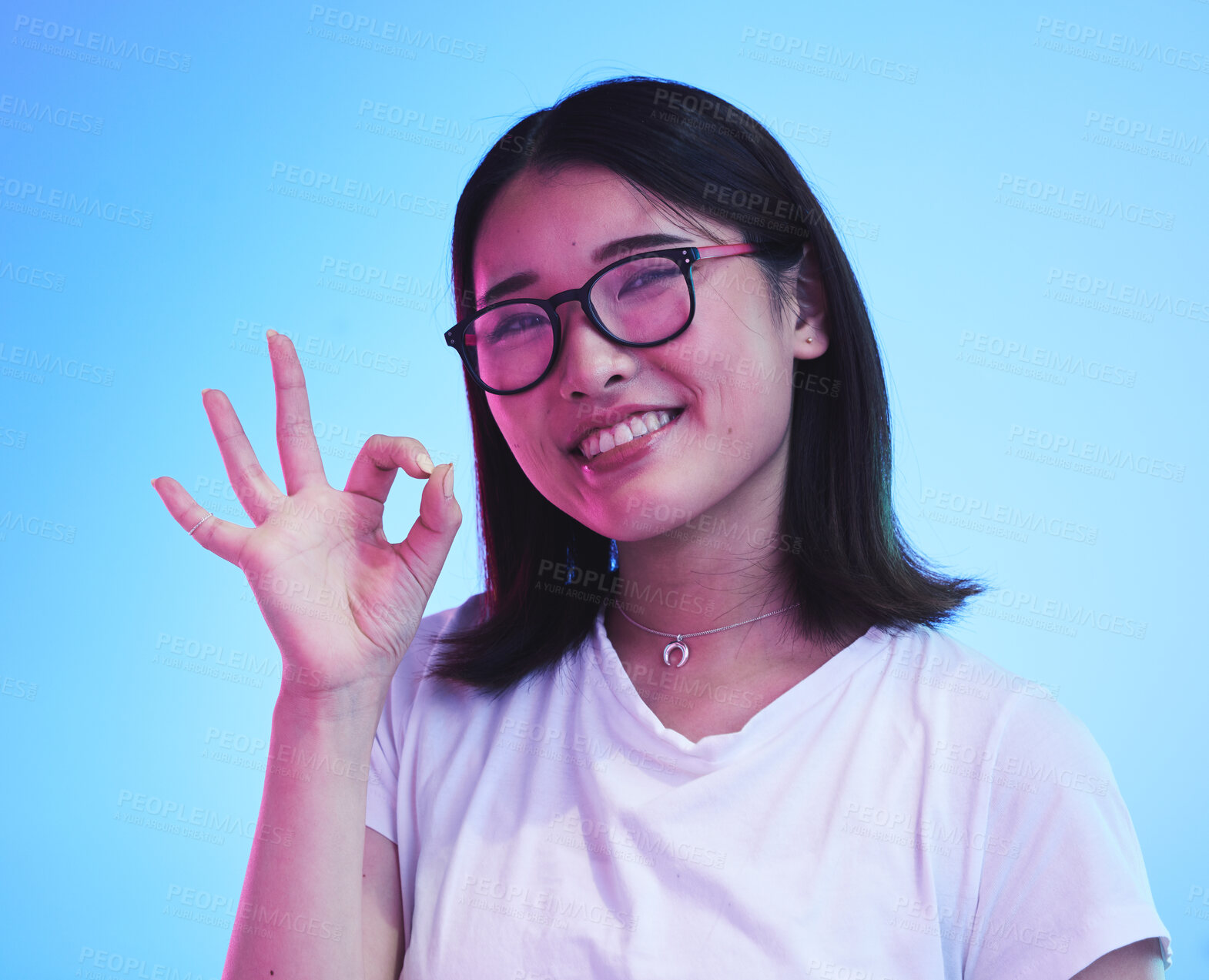 Buy stock photo Woman, okay hands or sign for learning success, certified and excellence in tshirt and a blue, studio background. Happy young, asian person in glasses, portrait and yes or support emoji for education