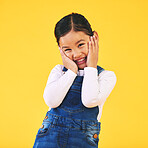 Portrait, smile and shy girl child in studio excited with news, announcement or fashion sale on yellow background. Happy, emoji and hands on face of sweet kid with promo, deal or toddler clothes info