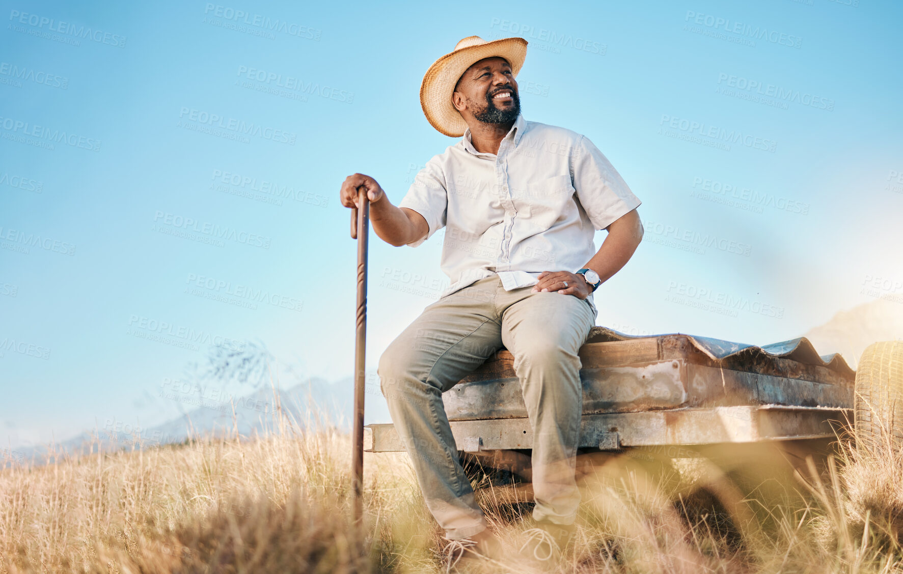 Buy stock photo Happy, African farmer and land in the countryside and man, sitting and watching over agriculture, field and environment. Farming, meadow and worker outdoor with smile in summer with happiness