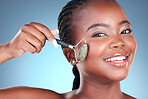 Portrait, beauty and black woman with roller, dermatology and skincare on a blue studio background.  Face, person and model with rose quartz, morning routine and cosmetics with treatment and grooming