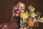 Aesthetic, beauty and protea with the face of a black woman in studio on brown background for natural treatment. Smile, plant or cosmetics and a young model indoor for skincare wellness with flowers