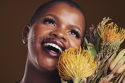 Buy stock photo Beauty, makeup and black woman with flowers in a studio for natural face cosmetics for self care. Happy, smile and young African model with protea floral aesthetic isolated by a brown background.