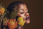Black woman, flowers and studio profile for beauty, wellness or thinking with protea by brown background. Girl, model and facial makeup for skin, sustainable cosmetics and eyes closed for aesthetic