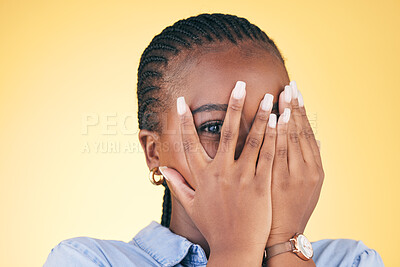 Buy stock photo Shy, black woman and hands on face peeping in studio isolated on yellow background. Portrait, fingers and African person embarrassed, scared at danger or fear at horror, social anxiety and spy hiding