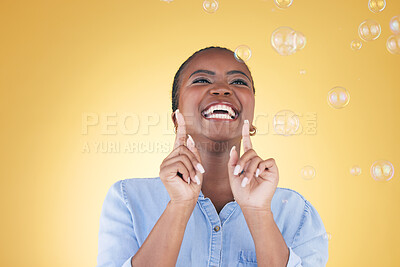 Buy stock photo Excited, happy and black woman on yellow background with bubbles for happiness, joy and fun. Playful laugh, smile and isolated African person in studio with soap bubble for freedom, magic and color