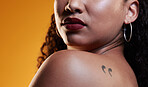 Beauty, makeup and a woman with a tattoo in studio for cosmetics, skin glow and dermatology. Closeup of a young female model on an orange background in studio with body art, confidence and comma ink