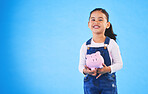 Girl child, piggy bank and studio portrait with mockup space, saving and financial education by blue background. Female kid, money box and happy with goal, investing and learning discipline with cash