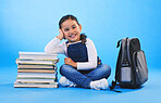 Girl child, sitting and books in studio portrait, backpack and excited for learning on floor by blue background. Female kid, education and development with smile, future and studying for knowledge