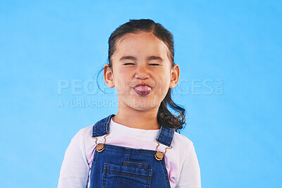 Buy stock photo Funny, face of child and girl with silly, goofy or facial expression on blue background in studio with fashion for children. Kid, portrait and tongue out of mouth in joke, humor or emoji for comedy