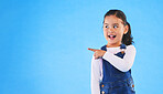 Pointing, blue background and child with mockup space for banner, advertising and promotion. Excited, happy and young girl in studio with hand gesture for discount information, announcement and news