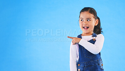 Buy stock photo Pointing, blue background and child with mockup space for banner, advertising and promotion. Excited, happy and young girl in studio with hand gesture for discount information, announcement and news