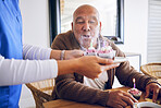 Celebration, blowing candles and a man with a caregiver, cupcake and birthday in a nursing home. Happy, house and a senior person or patient with cake or food from a healthcare employee for a party