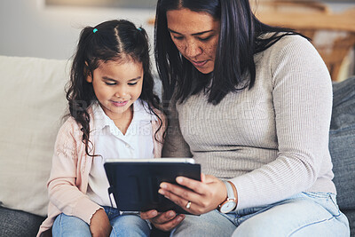 Buy stock photo Tablet, education and a mother on the sofa with her daughter in the living room of their home together. School, family or children with a mother and girl looking at an online homework assignment