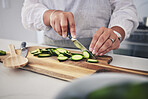 Cut, cucumber and hands cooking vegetable in a kitchen on a board or table in a home for hygiene as a chef. Salad, food and person prepare produce for a supper, lunch or dinner for diet meal