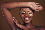 Gold, creative and art on black woman with makeup for beauty aesthetics isolated in studio brown background eyes closed. Smile, luxury and face of person with cosmetic glamour or design for skincare